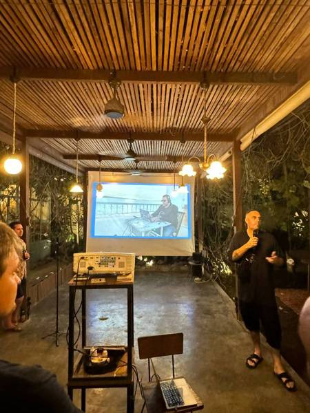 A speaker presenting to the room with slides behind them